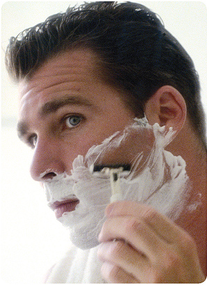 closeup of man with shaving cream on face using a razor